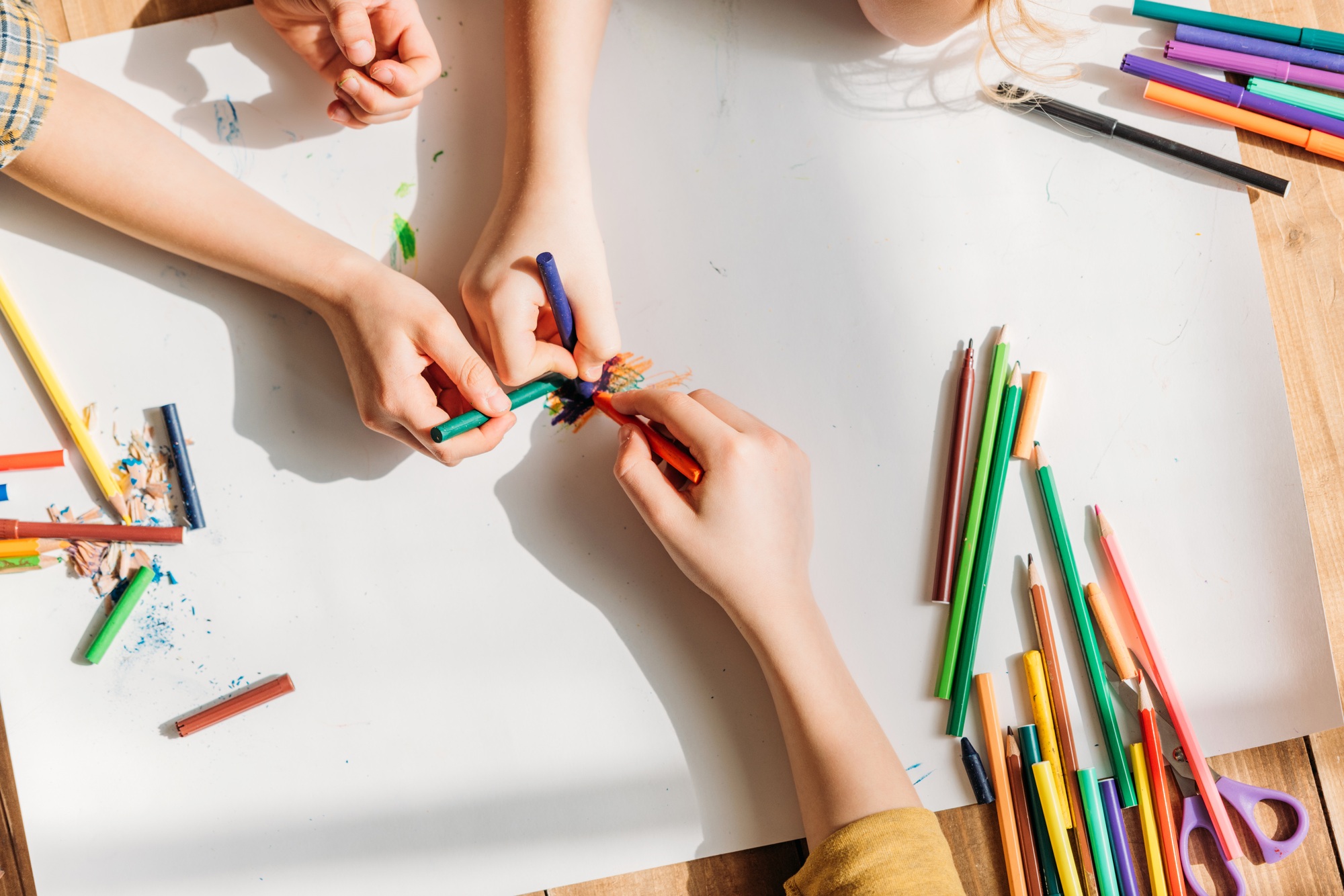 cropped view of cute kids drawing on paper with pencils while lying on floor