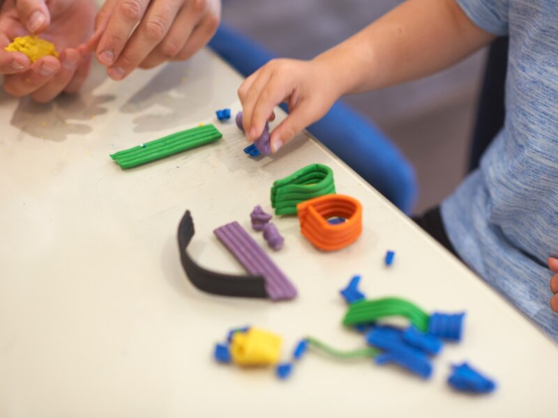 Father and son, sitting at table, playing with modelling clay, close-up