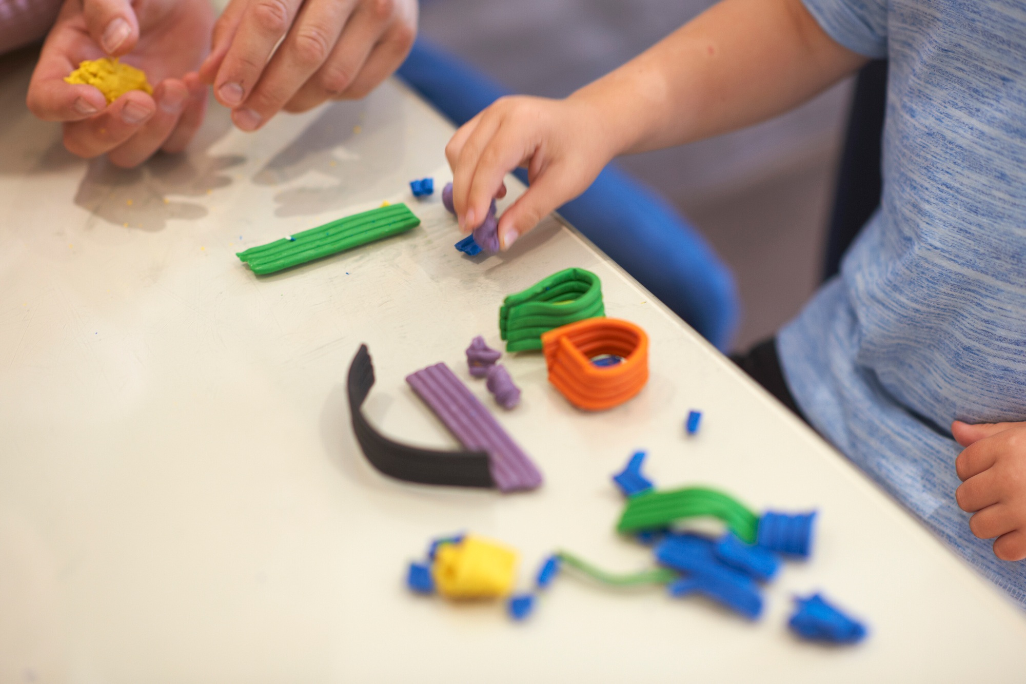 Father and son, sitting at table, playing with modelling clay, close-up