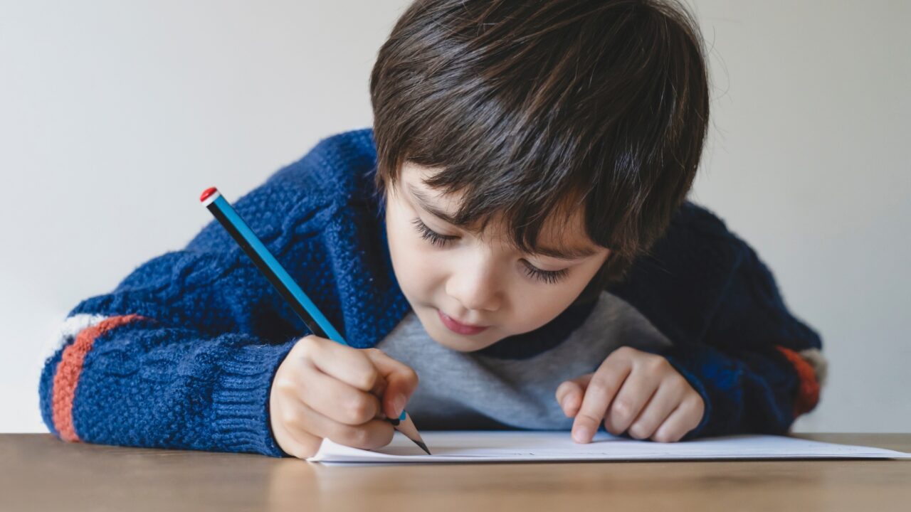 Kid using pencil writing the letter on white paper, Young boy drawing