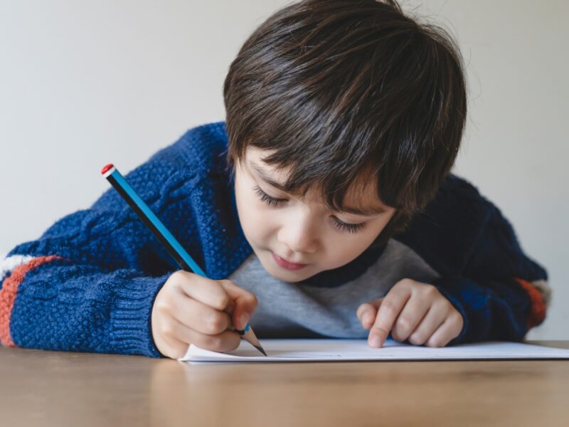 Kid using pencil writing the letter on white paper, Young boy drawing