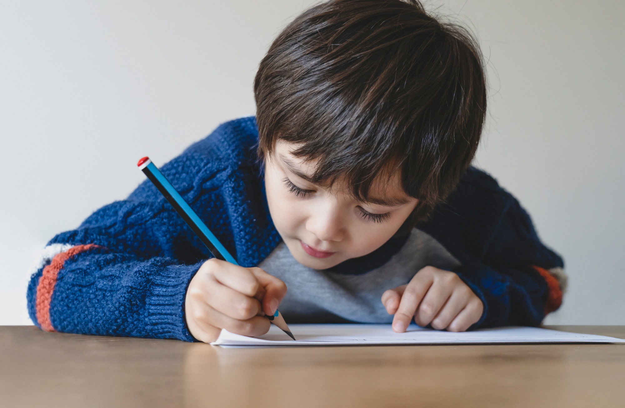 Kid using pencil writing the letter on white paper, Young boy drawing