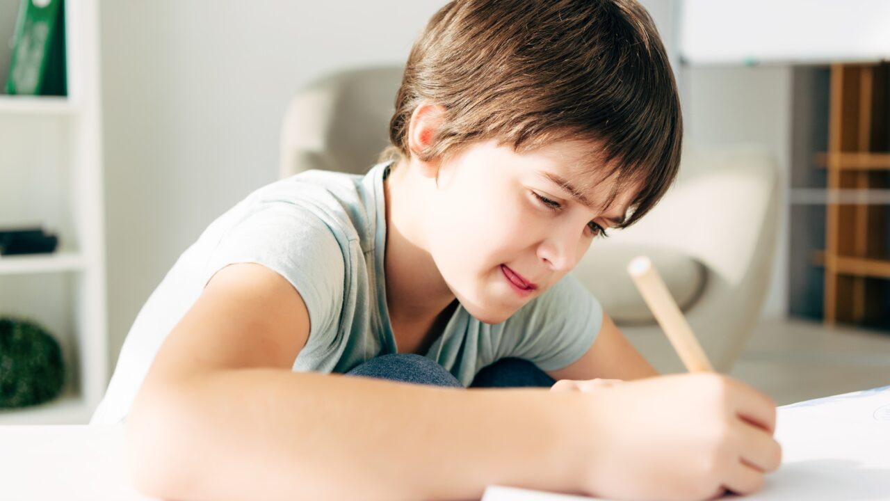 kid with dyslexia drawing with pencil and sitting at table
