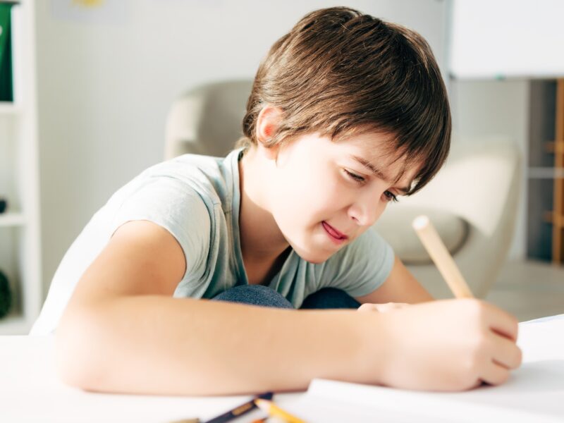 kid with dyslexia drawing with pencil and sitting at table