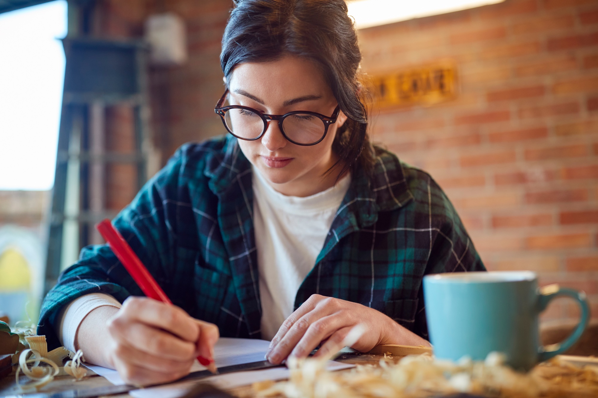 Young Female Carpenter Drawing And Measuring Woodwork Design In Garage Workshop
