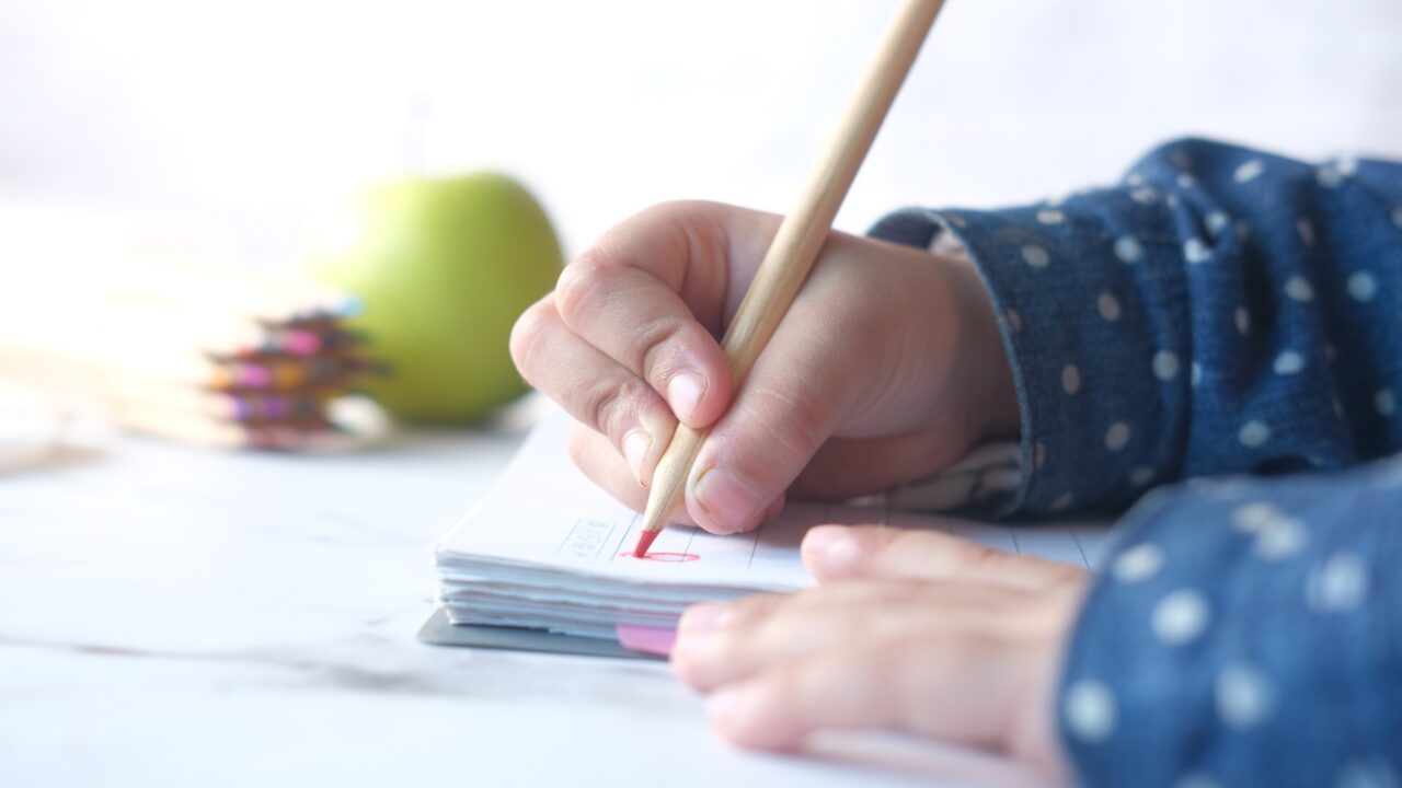 Close up of a child hand drawing with colored pencil on a page.