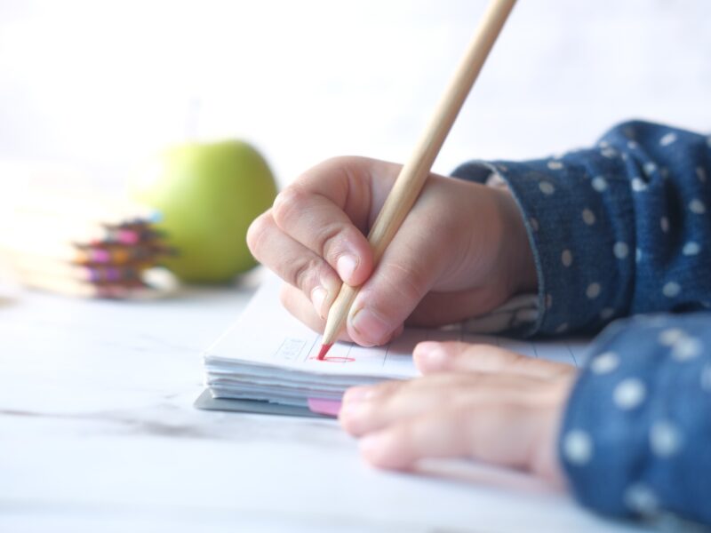 Close up of a child hand drawing with colored pencil on a page.