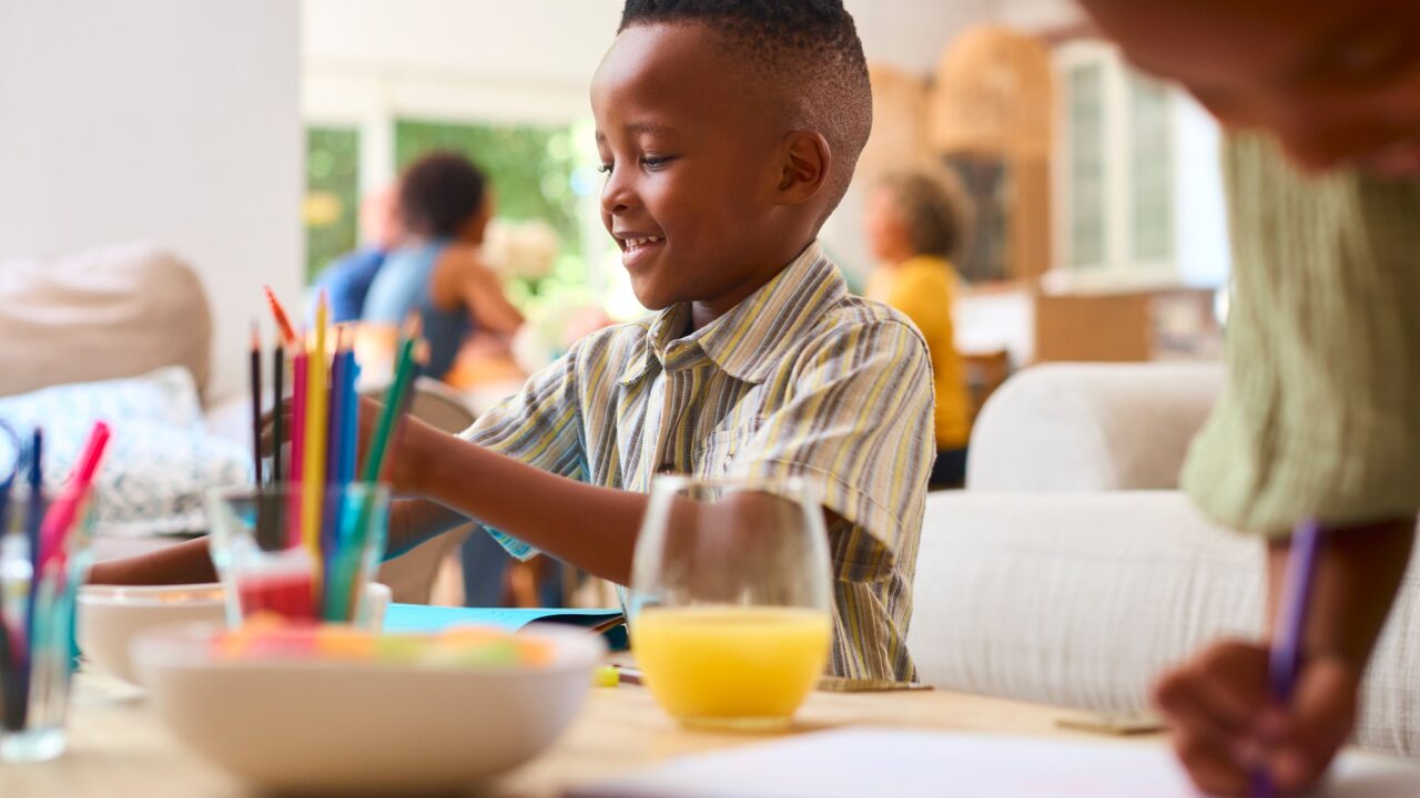 Grandchildren Indoors At Home Sitting At Table Drawing With Multi-Generation Family In Background