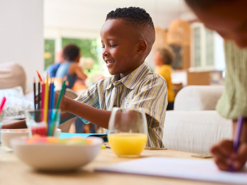 Grandchildren Indoors At Home Sitting At Table Drawing With Multi-Generation Family In Background