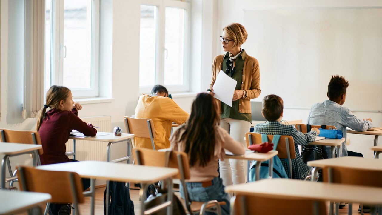 Mature teacher holding a class to group of school kids at primary school.