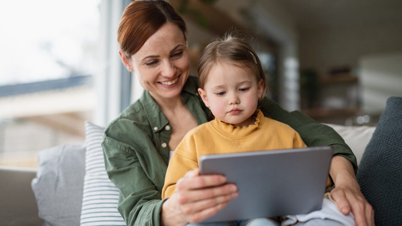 Mother with daughter watching kids programme on tablet indoors at home, single parenting concept.