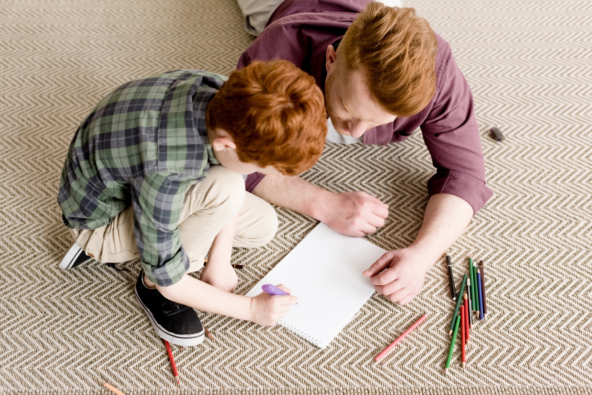 overhead view of redhead father and son drawing together on carpet