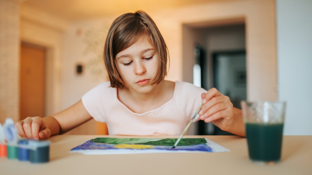 Serious beautiful concentrated girl sits at the table and draws, selective focus.