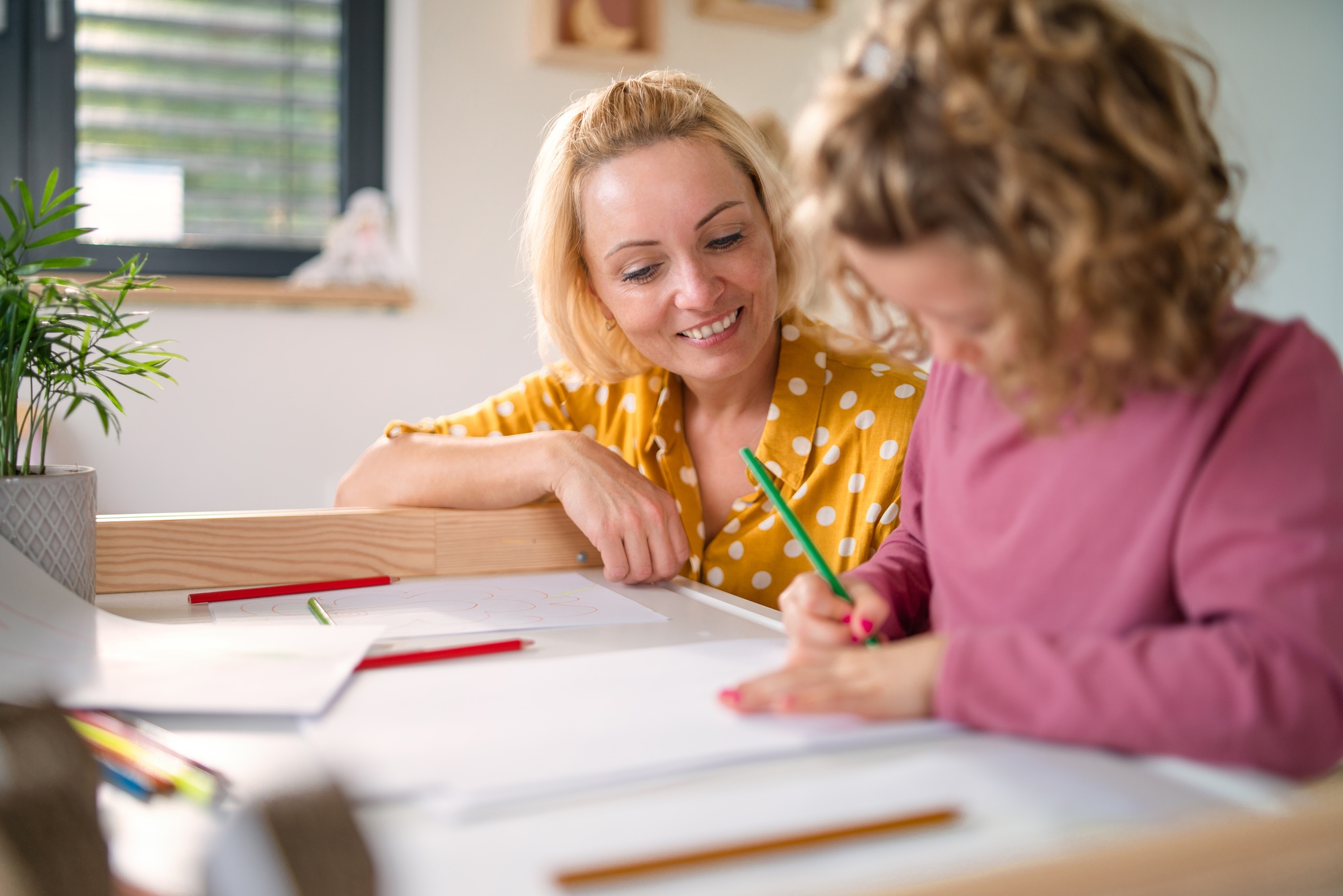 A cute small girl with mother indoors at home, drawing pictures.