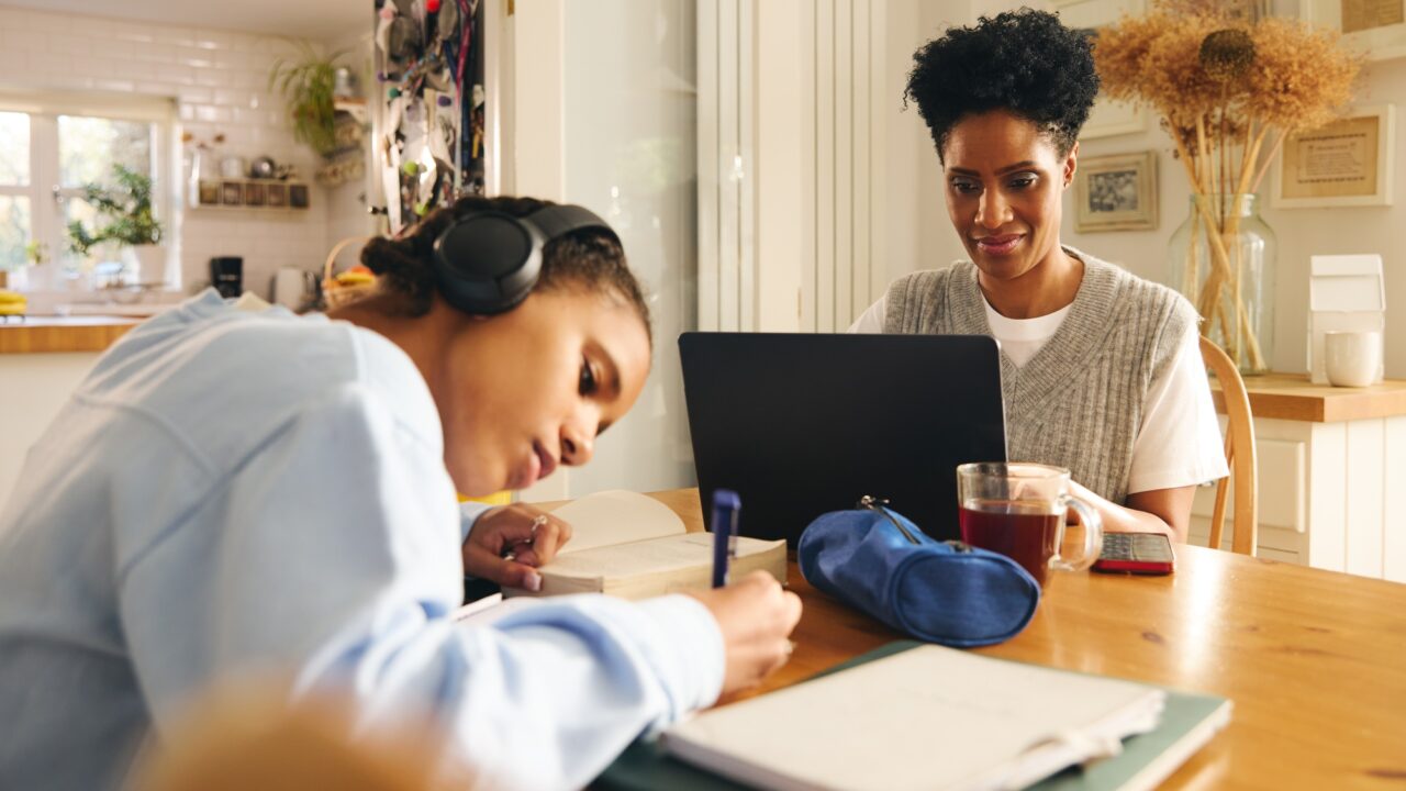 Daughter doing homework, mother working on laptop