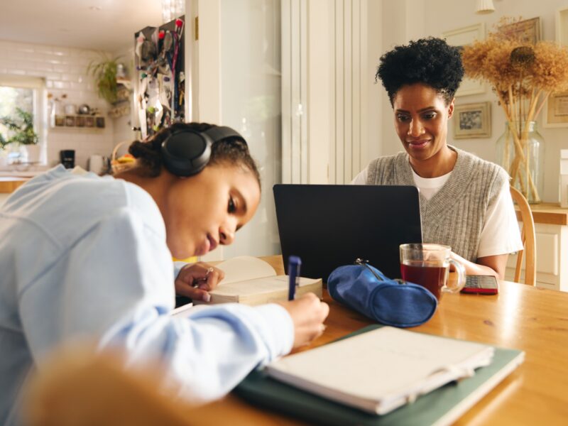 Daughter doing homework, mother working on laptop