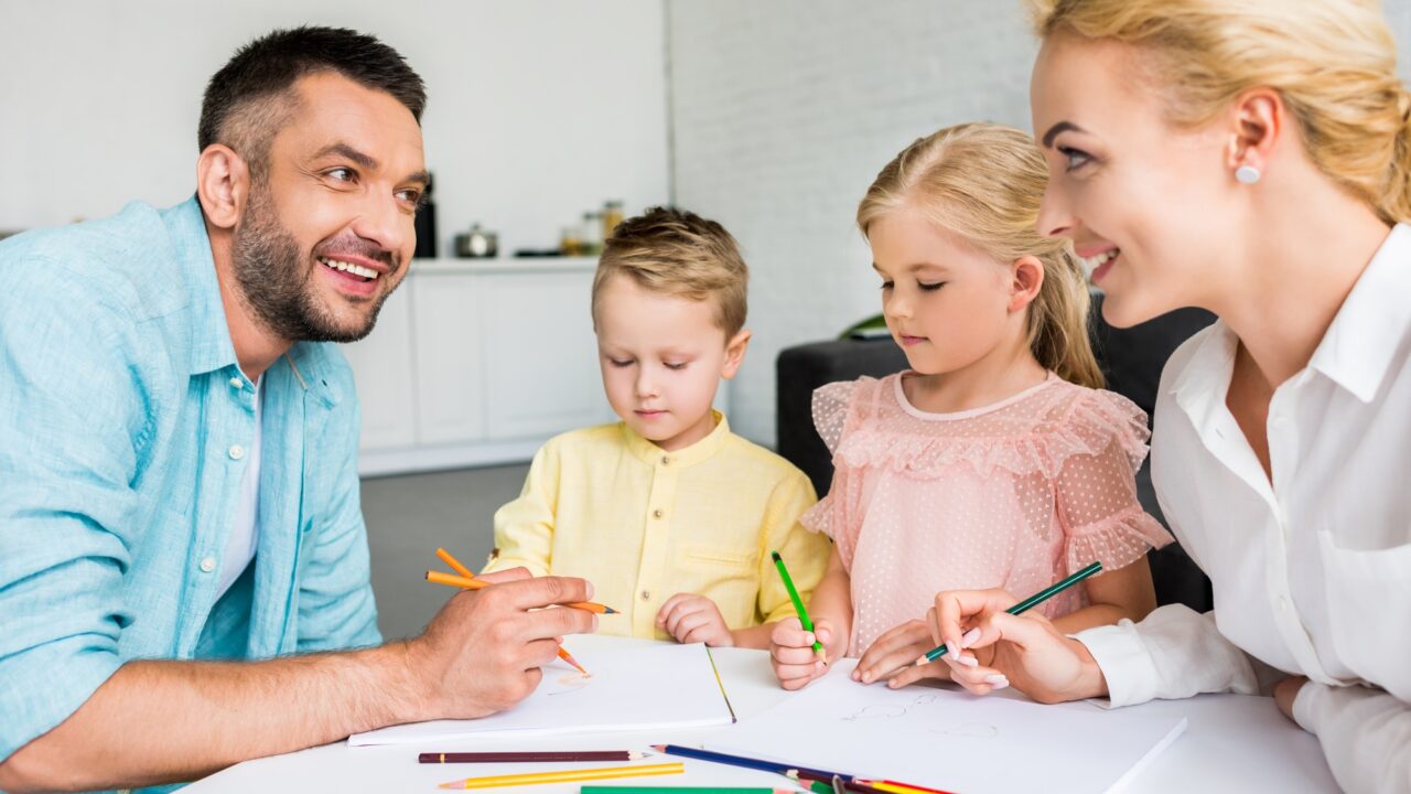 happy parents with two little kids drawing with colored pencils at home