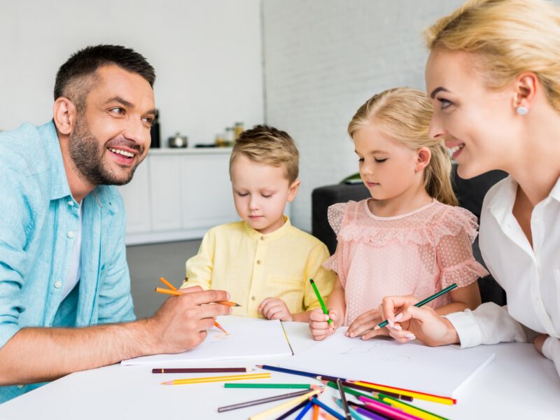 happy parents with two little kids drawing with colored pencils at home
