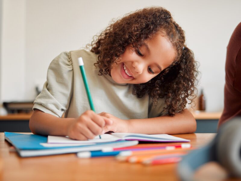Learning, smiling and creative young girl drawing with a colorful pencil feeling happy and content.