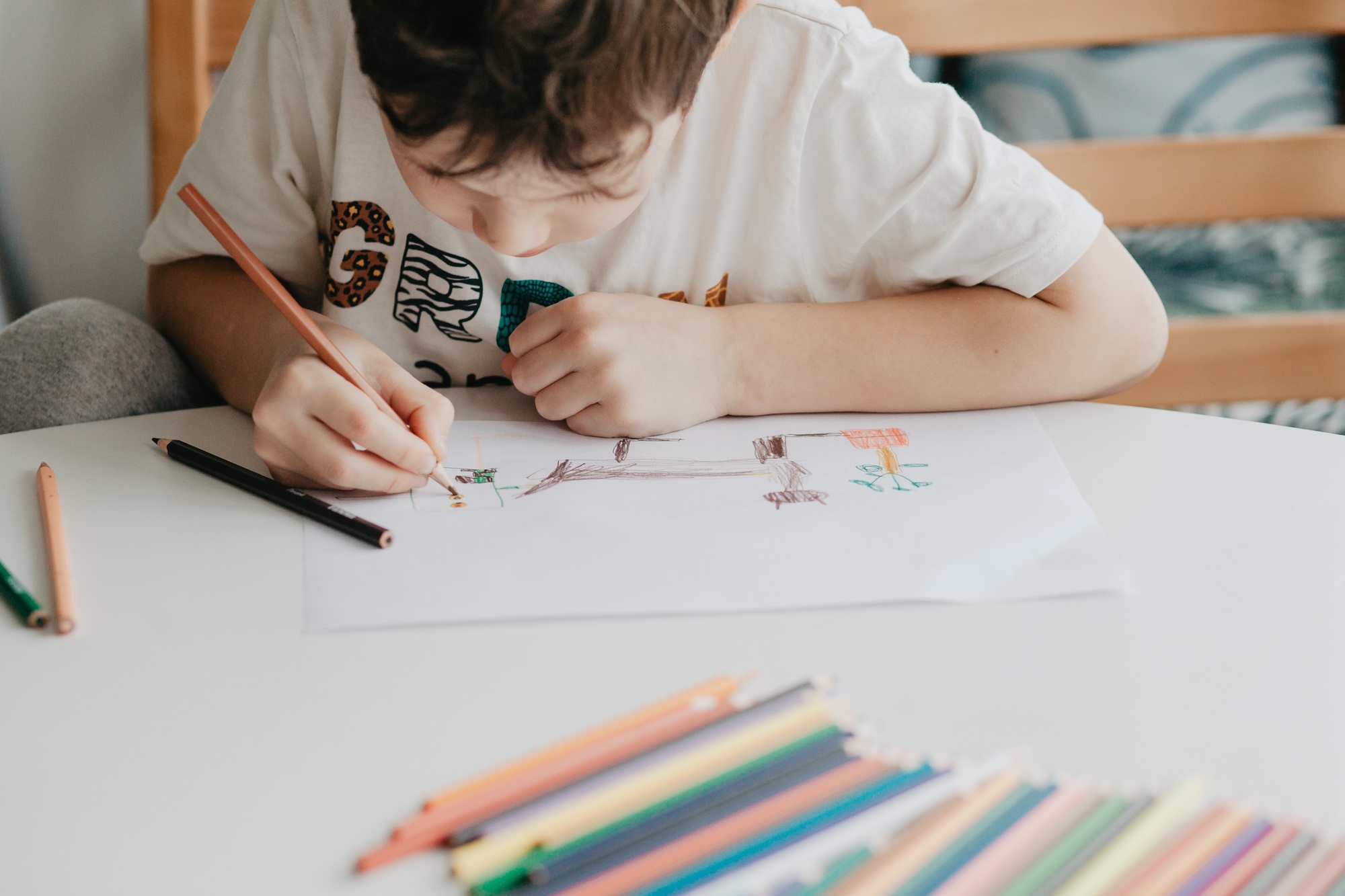 The boy draws with pencils at the kitchen